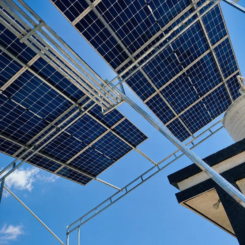 Upward view of the underside of an elevated solar array showing galvanized steel framing against blue sky