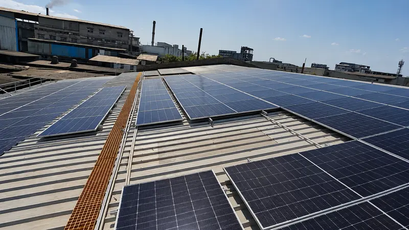 Solar panels installed flush on a corrugated metal factory roof with industrial buildings behind