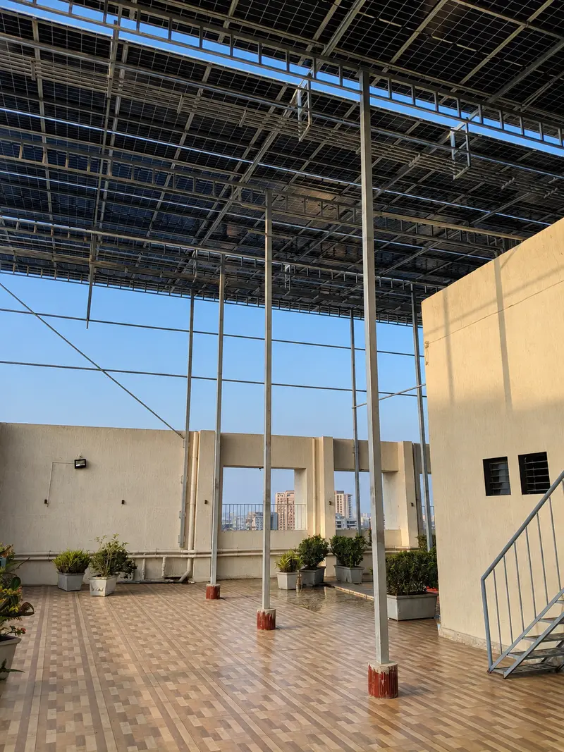 Tall elevated solar structure shading a tiled apartment terrace with plants and a staircase